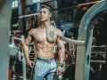 Muskulös man med tatueringar i gym. Han har en imponerande fysik, ett resultat av hårt arbete och att **deffa mat**.