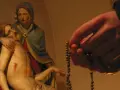 Eine Hand hält einen Rosenkranz, während die Pietà-Statue im Hintergrund zu sehen ist. Ein evangelischer Rosenkranz wird hier in Andacht gehalten.