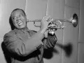 Louis Armstrong, znany jako "Satchmo", gra na trąbce z charakterystycznym uśmiechem.