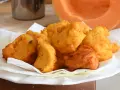 Frittelle di zucca dorate e croccanti, servite su carta assorbente, con una fetta di zucca sullo sfondo.
