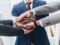 Zespół składa dłonie, symbolizując jedność i siłę. To jak prokura samoistna – wspólne działanie dla dobra firmy.