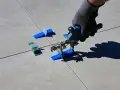 Mano con guanto usa pinza per livellare piastrelle, mostrando come tagliare piastrelle senza tagliapiastrelle con distanziatori.