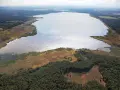 Rozległe jezioro Świerklaniec otoczone lasami i trzcinami, z widokiem na pola i zabudowania w oddali.