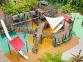 Ein riesiger, mehrstöckiger **Legoland Spielplatz** mit Rutschen, Kletternetzen und Holzbrücken, umgeben von grünen Bäumen.