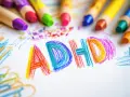 Kolorowe kredki otaczają napis "ADHD" narysowany na białej kartce. Dziecko, które nie jest neurotypowe, wyraża siebie przez sztukę.
