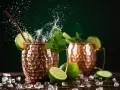 Dwa miedziane kubki z Moscow Mule i London Mule, ozdobione limonką i miętą, z bryzgami wody i lodem.