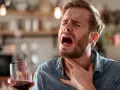 Mężczyzna z bólem gardła, trzymający kieliszek wina. Czuje nieprzyjemną zgagę po alkoholu.