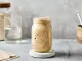 Ein Glas mit sprudelndem Sauerteig, angesetzt mit Dinkelmehl. Daneben ein Glas Wasser und ein Behälter mit Küchenutensilien.
