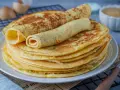 Ein Stapel goldbrauner Eierkuchen, zwei davon gerollt, perfekt für ein einfaches Eierkuchen Rezept.