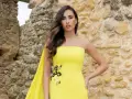 Mujer con vestido amarillo sin tirantes, con detalles florales y capa. Explora los diversos tipos de cuellos de vestidos.