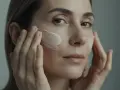 Une femme applique une crème sur son visage, étape essentielle du démaquillage. Ses doigts doux étalent le produit pour une peau nette et douce.