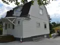 Vitt hus med ny fasad, stegar och material för byta fasad. En gul garagebyggnad syns i bakgrunden.