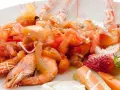 Scampi alla catalana: gamberi succulenti con pomodori freschi, cipolla rossa e una fragola decorativa. Un piatto colorato e invitante.