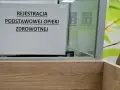 Tabliczka "Rejestracja Podstawowej Opieki Zdrowotnej" w poczekalni. Ubezpieczenie zdrowotne to podstawa.