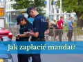 Dwóch policjantów w mundurach rozmawia, jeden z nich spisuje coś na kartce. W tle widać ludzi i budynki. Pytanie brzmi: "Jak zapłacić mandat?".