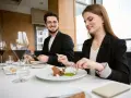 Elegancki strój na kolację do restauracji. Para w czarnych marynarkach delektuje się wykwintnym deserem przy kieliszkach czerwonego wina.