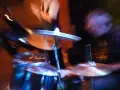Zbigniew Kucharski w akcji, grając na perkusji. Rozmyte światła i ruch tworzą dynamiczną scenę koncertową.