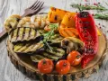 Grillowane warzywa: bakłażan, papryka, pieczarki, pomidorki i marchewka. Idealne dodatki do grilla, podane na drewnianej desce.