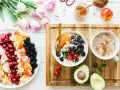 Un bol de yaourt aux fruits rouges, myrtilles et amandes, un plateau de fruits frais, un avocat et une tasse de café. Un repas sain, un aliment anti inflammatoire.