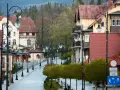 Ulica w Świeradowie Zdroju z zabytkowymi kamienicami i latarniami. Wiosenne drzewka tworzą zielony szpaler, zapraszając do odkrywania atrakcji.