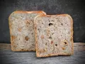 Zwei Scheiben salzarmes Brot mit Nüssen liegen auf Holz.