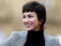 Uśmiechnięta kobieta z charakterystyczną fryzurą bixi, w czarnym golfie i wzorzystej marynarce.