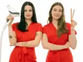 Dwie kosmetyczki w czerwonych uniformach. Jedna trzyma depilator, druga patyczki do wosku. Dowiedz się, ile kosztuje depilacja woskiem u kosmetyczki.