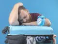 Zmęczony podróżnik śpi na walizce obok budzika. Czy to jetlag?