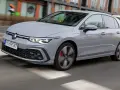 Szary Volkswagen Golf GTE porusza się po miejskiej drodze, z rozmytym tłem budynków i przechodniów.