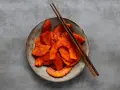 Miseczka z pokrojonym kimchi i pałeczkami na szarym tle.