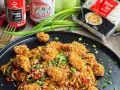 Pyszny makaron udon z kurczakiem w panierce i kolorowymi warzywami, posypany sezamem i szczypiorkiem.