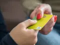 Eine Hand gibt einer anderen eine gelbe Girocard. Dies könnte die erste kinder debitkarte sein, die ein Kind erhält.