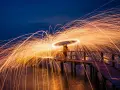 Une personne sur un pont crée une **light painting photo** spectaculaire avec des traînées de feu dans le ciel nocturne.