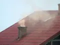 Dym z komina, unoszący się nad czerwonym dachem, niesie ze sobą zapach palonego drewna i trochę sadzy.