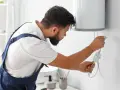 Tecnico con tuta blu controlla la caldaia. La manutenzione caldaia a chi spetta? Al tecnico specializzato, per la sicurezza di tutti.