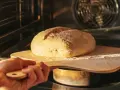 Ręka wsuwa drewnianą łopatą bochenek chleba do rozgrzanego piekarnika. To kulminacyjny moment wyrabiania ciasta na chleb.