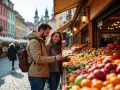 Para młoda sprawdza ceny w Czechach na targu z owocami. Kolorowe kamienice w tle.