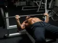 Man med skägg och synliga muskler utför bänkpress som en del av sitt starting strength program.