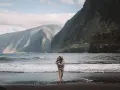 Kobieta z dzieckiem na rękach na plaży, w tle majestatyczne góry i ocean. Niezapomniane madera widoki.