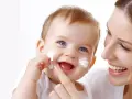 Uśmiechnięta mama delikatnie nakłada sudocrem na twarz swojego radosnego dziecka.