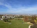 Jesienny widok na Kraków z Kopca Kraka. Ludzie odpoczywają na trawie, podziwiając panoramę miasta i kolorowe drzewa.