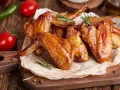 Alette di pollo dorate e succulente, cotte alla perfezione nella friggitrice ad aria, servite su carta forno con rosmarino, pomodorini e peperoncino.