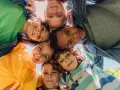 Un groupe d'enfants souriants forme un cercle, leurs visages se rejoignant au centre. Leurs regards joyeux et leurs expressions témoignent d'un bel encadrement d'enfants.