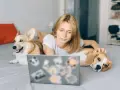 Ragazza con due cani sul letto, uno corgi e un beagle, che guarda un laptop. Un esempio di come lavorare con gli animali in modo sereno.