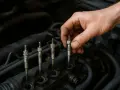 Dłoń mechanika wykonuje wymianę świec żarowych w silniku diesla.