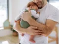 Ojciec czule tuli noworodka, podnosząc go pod pachy. Od kiedy tylko się urodził, czuje tę niezwykłą więź.