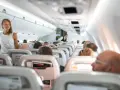 Widok wnętrza samolotu z pasażerami siedzącymi w rzędach i stewardesą.