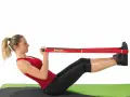 Femme faisant un exercice avec un élastique, jambes tendues et mains tenant la bande rouge.