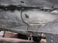 Underneath a car, dark fluid is leaking from a seam. A small puddle of blue fluid is visible, suggesting a coolant leak.