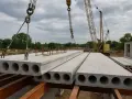 Strop z płyty żerańskiej jest podnoszony przez dźwig na budowie. W tle widać inne płyty i konstrukcje budowlane.